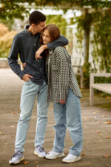 Fototapeta premium Young Cute Female Hugs Boyfriend. In Autumn Outdoor. Lovers Walking in Park. Attractive Funny Couple. Lovestory in Forest. Man and Woman. Cute Lovers in the Park. Family Concept. Happy Couple.