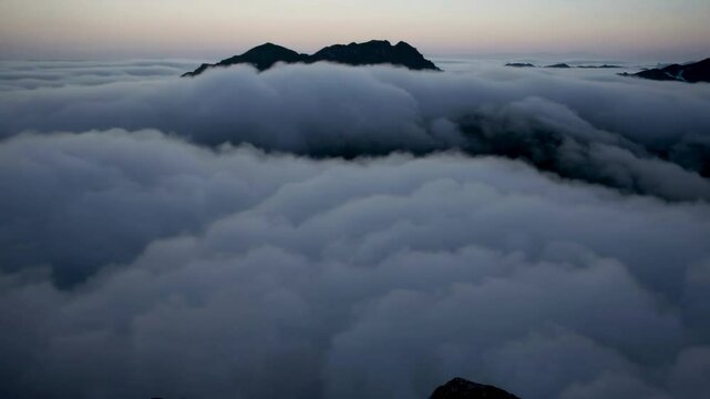 The mighty peaks of the mountains rise above the boundless sea of clouds, like islands in the celestial ocean, in the predawn haze