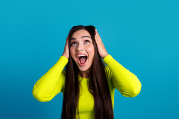 Energetic young woman in a vibrant yellow top expressing excitement against a bright blue...