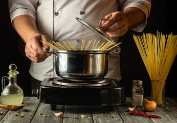 A chef skillfully prepares spaghetti, placing the long strands into a boiling pot on a stove....