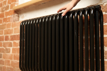 The hand touches the battery. There is a problem with central heating in the house. A woman checks the radiator in a cold apartment. High quality photo