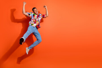 Young man in vibrant shirt jumping with joy against an orange backdrop, expressing freedom and...