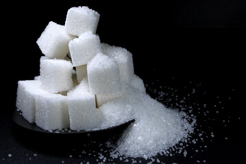 pressed sugar in the form of white cubes and granulated sugar scattered on a black surface