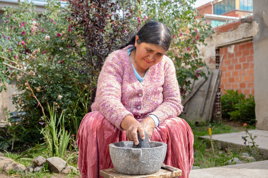 old woman of the aymara chola culture grinding in a mortar or also called batan in the courtyard of her house in la paz, bolivia - cooking concept