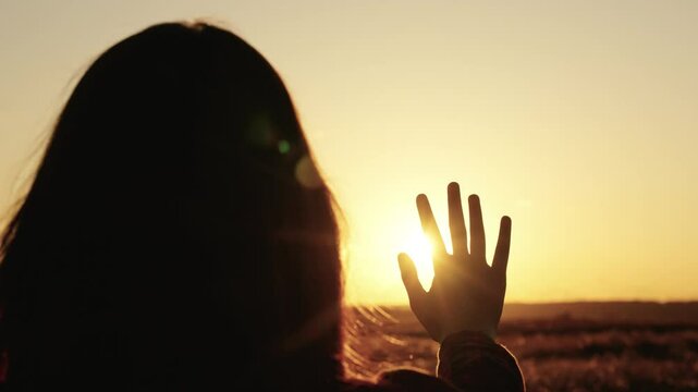 Woman reaching out with her hand to the sun, silhouette of a woman's hand in sun glare, silhouette of girl in sunlight, girl praying in the sun, traveler rejoicing in sunset, asking God for help