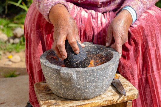 hands of old woman of the aymara chola culture grinding in a mortar or also called batan in the courtyard of her house in la paz, bolivia - cooking concept