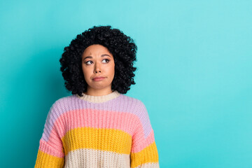 Young stylish woman with curly hair expressing a thoughtful attitude against turquoise background