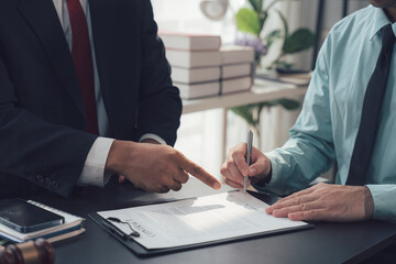 Formal Contract Signing: Two business professionals sit at a desk, one pointing at the document as...
