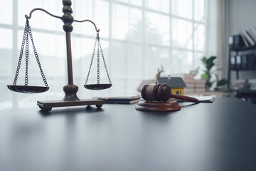Scales of Justice: A wooden gavel rests next to a miniature house and a set of scales of justice on...