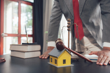 Justice for the Home: A lawyer in a gray suit and red tie stands resolutely over a miniature house,...