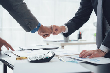 Fist Bump of Success: A dynamic image of two business professionals exchanging a fist bump over a desk, symbolizing their agreement and shared goal. The desk is covered in paperwork, a calculator.