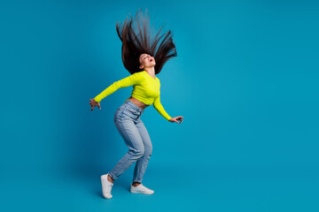 Young stylish woman in a yellow top and jeans dancing joyfully while flipping her long brunette...