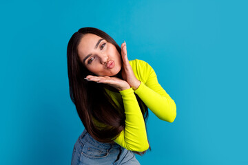 Trendy young woman posing playfully with a kiss in a vibrant outfit on a bright blue background