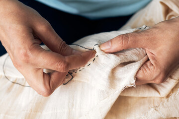 Close-up of hands stitching fabric with detailed embroidery, using a needle and thread on white...
