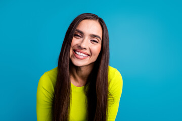 Smiling young woman in a bright yellow top against a vibrant blue background, expressing happiness...