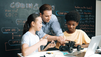 Caucasian teacher looking at laptop screen while explain car model system at blackboard with coding...