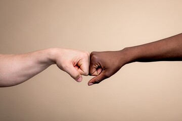 Two hands fist bumping, symbolizing unity and friendship. Diverse hands, one light-skinned, one dark-skinned, emphasize connection and solidarity. Diversity and unity concept, equality and connection.