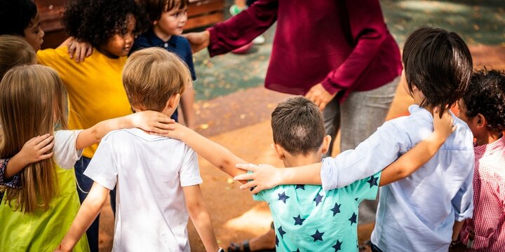 Children playing in a circle outdoors, diverse group of kids, arms around each other, enjoying playtime, diverse children, outdoor fun, group play, kids together. Diverse school kids at playground.