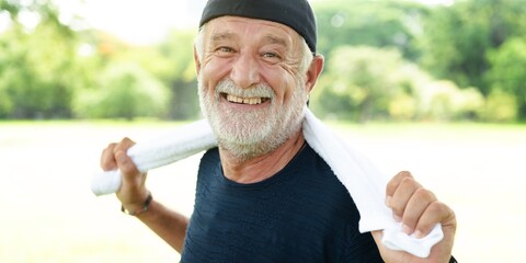 Elderly man smiling outdoors, holding a towel. Happy elderly man enjoying nature. Elderly man with...
