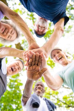 Diverse group of seniors in a circle, hands stacked, smiling outdoors. Elderly friends, teamwork, unity. Happy seniors, diverse group, teamwork, unity. People stacking hands, unity and teamwork.