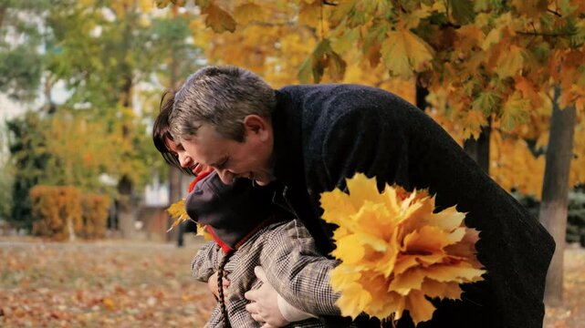 Kids clutching fall foliage in hands sprint toward mother and father in urban park. Children embrace parents holding autumn leaves. Boy and girl having hands with maple leaves revel with parents