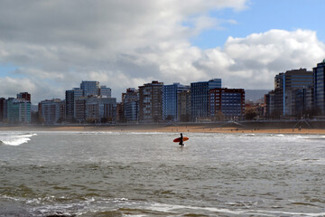 Surfer in cantabrian sea with urban skyline in northern Spain. Gijon, Asturias. Bay of Biscay