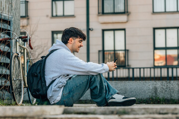 young man or student with mobile phone sitting on the street with backpack and bicycle