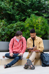 Happy young man with Down syndrome and mentoring friend sitting and talking outdoors, spending time...