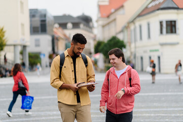A young man with Down syndrome and his mentoring friend walking across city, talking.
