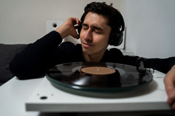 Emotional music lover is listening a vinyl record on a turntable player. Cheerful hipster is listening to music by vintage vinyl records and feeling real emotions of music lover.