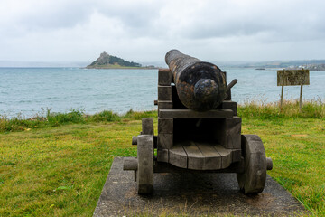 Old rusting cannon on wooden carriage aimed at castle on Cornish coast. England coastal history.