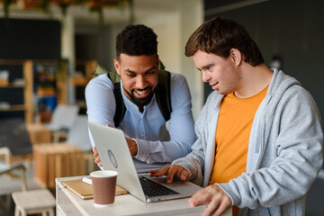 Happy young man with Down syndrome and his tutor using lapotp indoors at school.