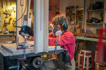 Carpentry workshop, craftsman master working. Concentrated man wear ear muffs, protective glasses works with cnc woodworking milling machine. Manual wood milling guy holds tool controlling process