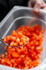 Diced red tomatoes in a clear container, with a spoonful being lifted. Fresh ingredients suitable for cooking or salads, showcasing vibrant colors and textures. Clean, appetizing presentation.