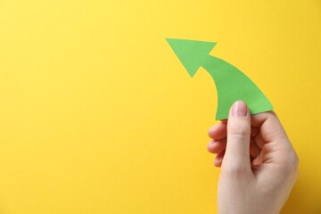 Woman with paper arrow on yellow background, top view. Space for text
