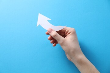 Woman with paper arrow on light blue background, top view. Space for text