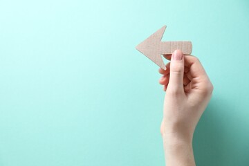 Woman with paper arrow on turquoise background, top view. Space for text