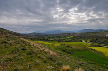 Naklejka premium Overcast hills reveal vibrant fields in a quiet valley under a dramatic sky