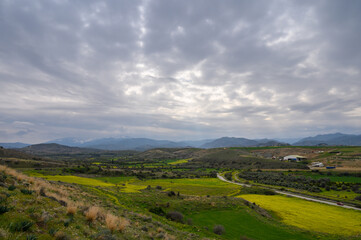 Fototapeta premium Lush countryside stretches under a cloudy sky with vibrant fields and distant mountains in the background