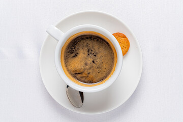 Rich Espresso Filled Cup Stands Elegantly on a Pristine White Plate Accompanied by a Crispy Biscuit, Inviting Warmth and Comfort on a Serene Afternoon.