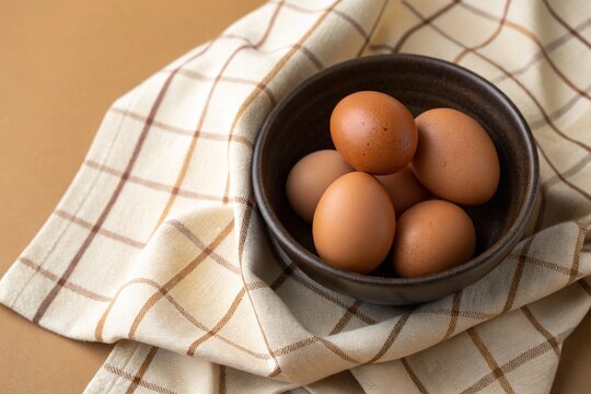 Fresh brown eggs in a rustic ceramic bowl on a checkered kitchen cloth