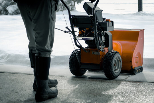 person walking out of garage with snowblower after a weather event. man wearing tall black snow boots.