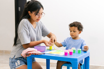 Latin american mother helping her son painting at home