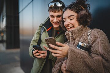 young couple stand and use cellphone in front black wall outdoor