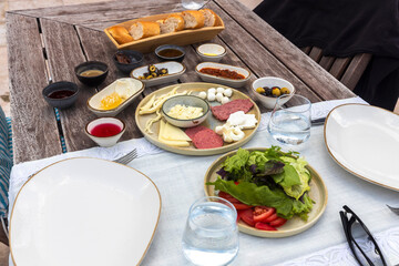 Turkish breakfast with an omelet, french fries, croissants, jam, fresh coffee, honey, tea, vegetables, and salad on a wooden table on the terrace.