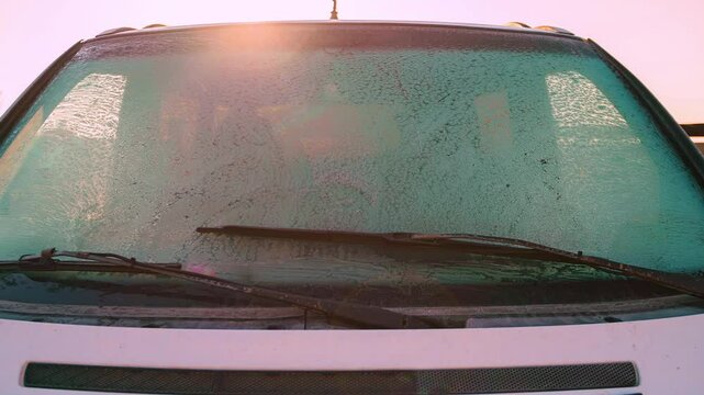 ,Frozen Windshield at Sunrise: Ice Crystals on Car Glass Obscure the Interior View