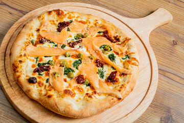 Deliciously Crafted Thin-Crust Pizza Topped With Smoked Salmon, Kale, Sun-Dried Tomatoes, and a Creamy Sauce Served on a Rustic Wooden Board.
