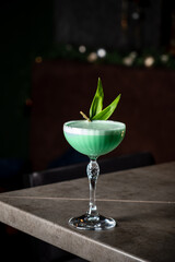 Vibrant Green Cocktail Garnished With Fresh Leaves Captivating Guests at a Stylish Bar During a Lively Evening Gathering.