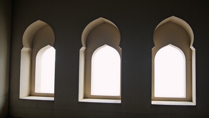 A white shadow of three arched mosque window silhouettes on a wall