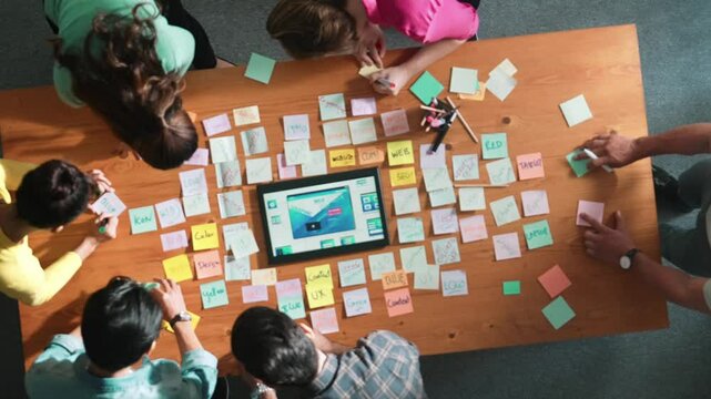 Top down view of programmer brainstorming and planning about web design while looking at tablet wireframe prototype. Aerial view of skilled developer team talking about digital application. Symposium.